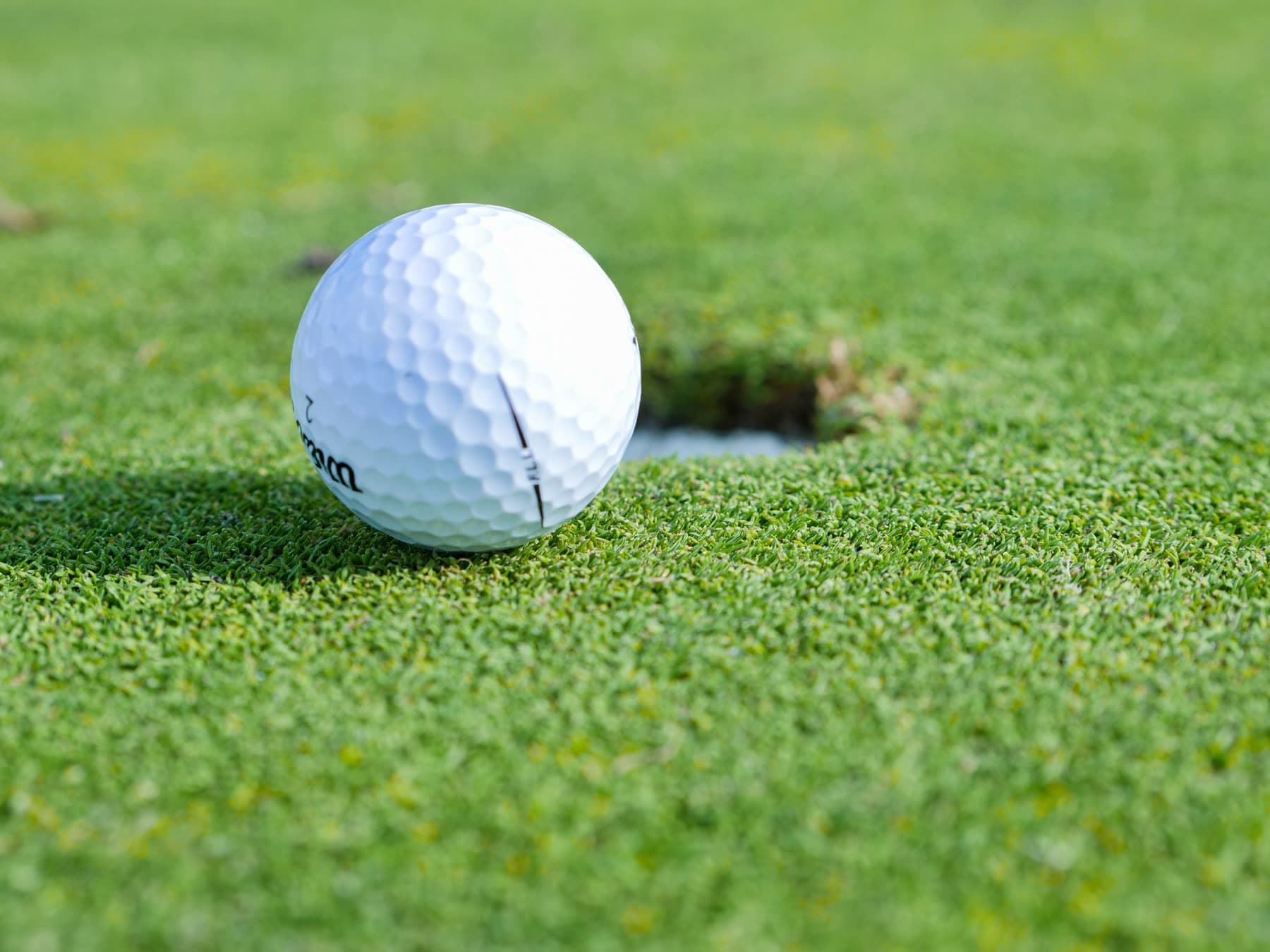 A golf ball on the fringe, a few feet from the hole, with a bunker behind it.